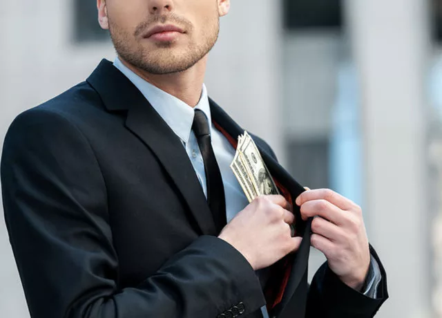 Man in suit hiding money in jacket to illustrate white collar crime investigations